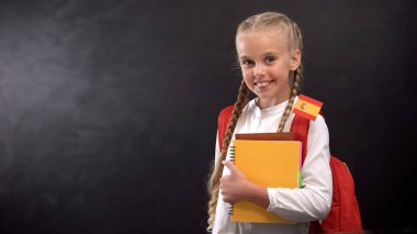 Küçük İspanya bayrağı ile kitap tutan neşeli öğrenci, yabancı dil öğrenmeye hazır