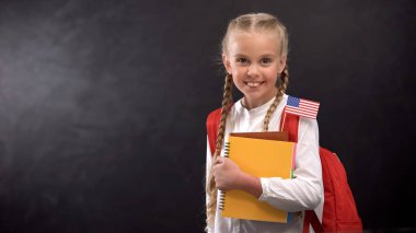 Küçük Abd bayrağı ile yabancı dil öğrenmeye hazır kitap tutan sevimli kız öğrenci