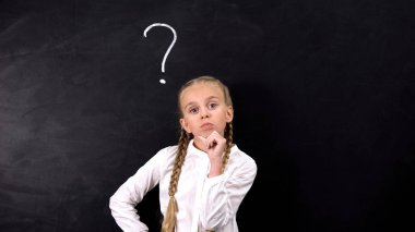 İlkokul öğrencisi görev çözmeye çalışıyor, tahtaüzerinde soru işareti