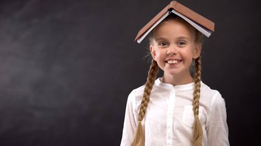 Kameraya bakarak, molada eğlenmek, şaka yaparken, başında kitapla gülümseyen kız