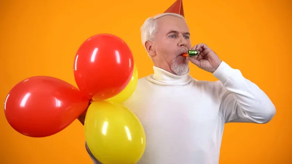 Ευτυχής Αρσενικό Συνταξιούχο Χρησιμοποιώντας Φυσητήρας Κόμμα Και Κρατώντας Πολύχρωμα Μπαλόνια — Φωτογραφία Αρχείου