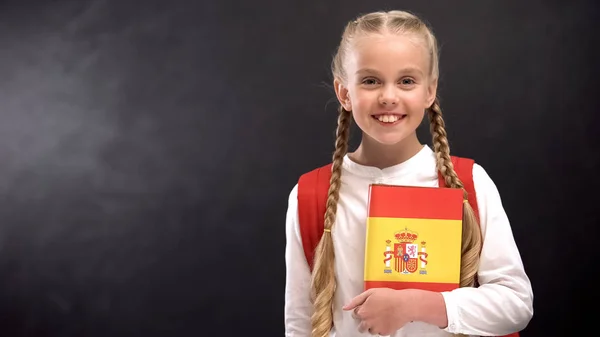 Lachende Schoolmeisje Houdt Spaanse Taal Boek Tegen Blackboard Achtergrond — Stockfoto