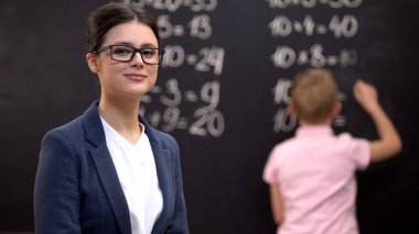 Genç kadın öğretmen kamera bakıyor, matematik egzersizleri çözme okul çocuğu, iş