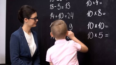 Akıllı öğrenci kara tahta üzerinde matematik egzersizleri çözme, öğretmen yanında duran