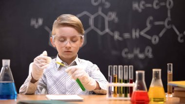 Koruyucu gözlüklü çocuk tüpe kimyasal madde döküyor, reaksiyonu kontrol ediyor
