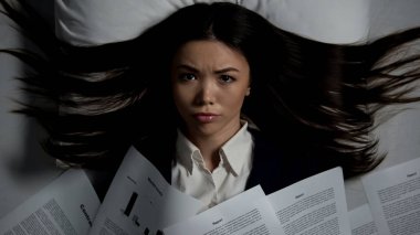 Stresli kadın yatakta yatan belgelerle kaplı, son teslim tarihi, kötü rüya