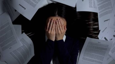Korkmuş kadın yüzünü kapatıyor, evrak yığınları arasında yatıyor, işe başlamaktan korkuyor