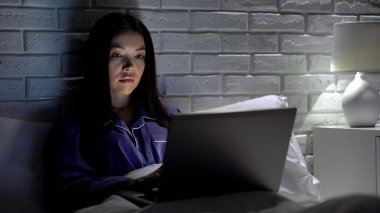 Yatakta yatan kadın dizüstü bilgisayarda aceleyle çalışıyor, son teslim tarihini karşılamaya çalışıyor, mesai saatleri