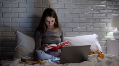 Genç anne kitap okuyor, oyuncaklar arasında yatakta oturuyor, yetiştirme yöntemleri