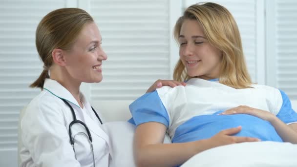 Улыбающаяся акушерка и беременная женщина в больничной койке, смотрящая в камеру, пренатальный уход — стоковое видео