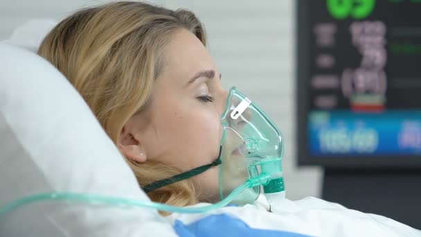 女病人躺在病床上戴氧气面罩，监视器显示生命体征 — 图库视频影像