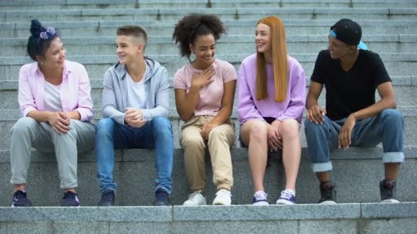 Група багатоетнічних молодих людей, які сидять на сходинках академії, час дозвілля — стокове відео