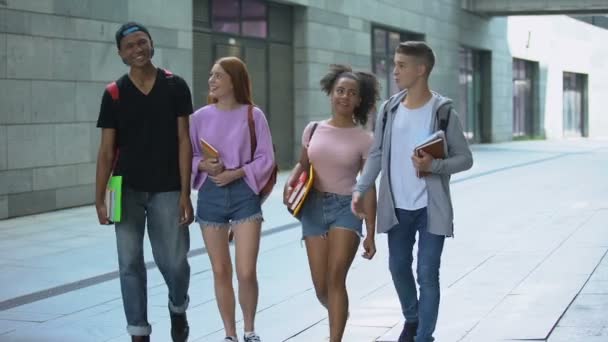 Estudiantes multiétnicos con libro caminando cerca del campus durante las clases — Vídeos de Stock