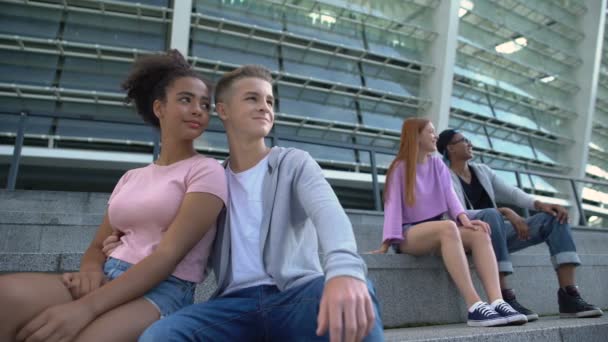 Dos parejas multirraciales de adolescentes sentados escaleras al aire libre, jóvenes románticos — Vídeo de stock