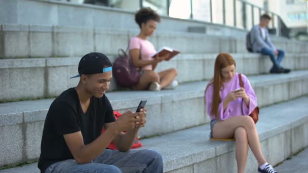 Vrolijke mannelijke tiener chatten smartphone buitenshuis, middelbare scholieren op pauze — Stockvideo