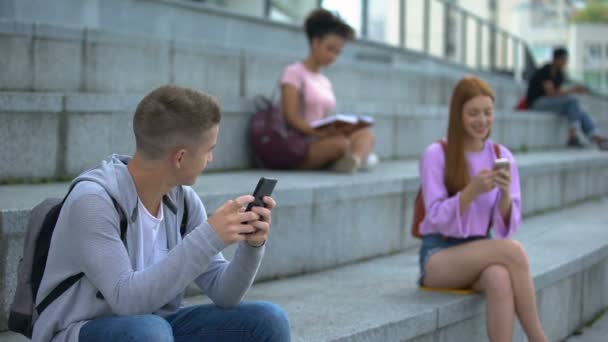 Hombre hembra adolescentes charlando teléfono inteligente sentado al lado, la comunicación en línea — Vídeo de stock