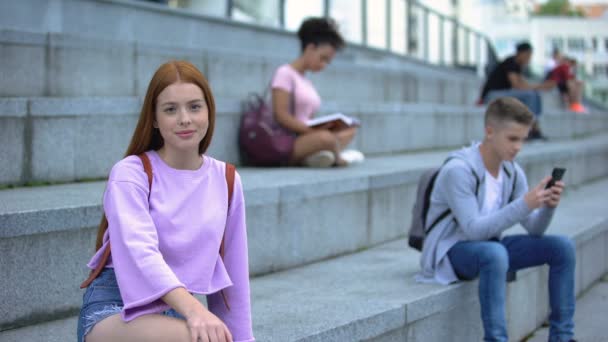 Vackra rödhårig tonåring sittande trappor leende kamera, studentutbyte — Stockvideo