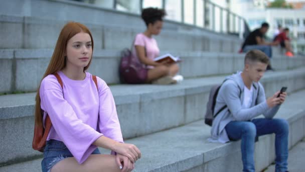 Грустная студентка, сидящая одна на ступеньках кампуса, необщительные подростковые проблемы — стоковое видео