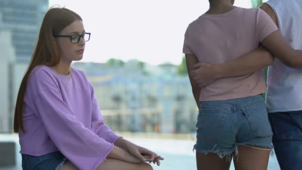 Lonely female teenager looking at happy loving couple passing by on street — Stock Video