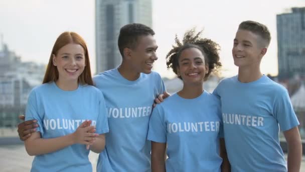 Χαμογελαστοί νεαροί εθελοντές με μπλουζάκια που αναζητούν κάμερα, κοινωνική ομαδική εργασία, βοήθεια — Αρχείο Βίντεο