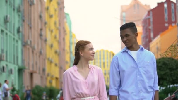 Giovane coppia che cammina per strada tenendosi per mano e timidamente guardando l'un l'altro, data — Video Stock