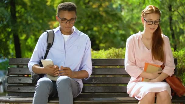 Funny teenagers in glasses moving closer to each other sitting on bench, liking — Stock Video