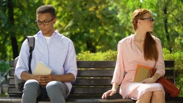 Estudiantes multirraciales tomados de la mano sentados en el banco en el parque, primera cita de geeks — Vídeo de stock