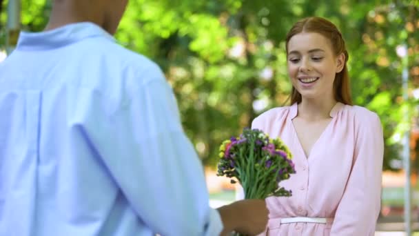 Mixta-raza adolescente chico presentando flores a sorprendido novia, fecha en parque — Vídeos de Stock