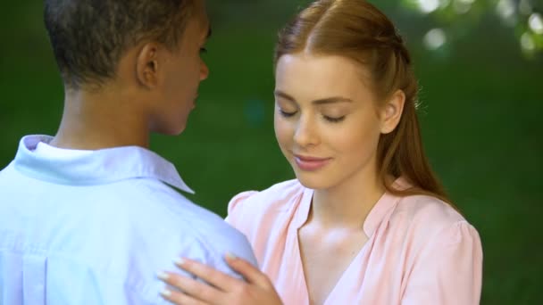 Adolescente menina ternamente abraçando seu namorado afro-americano no parque ensolarado — Vídeo de Stock