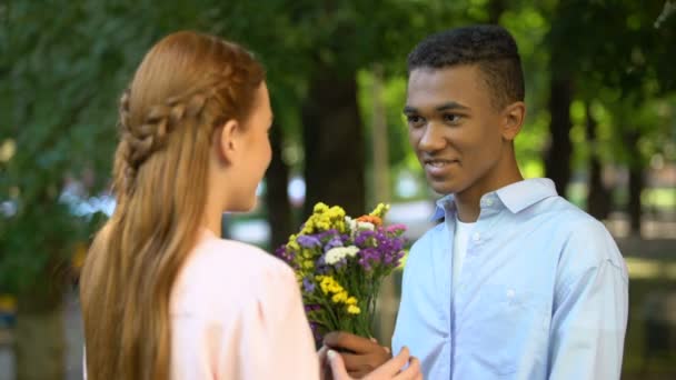 Doce menino adolescente afro-americano apresentando um monte de flores para namorada tímida — Vídeo de Stock