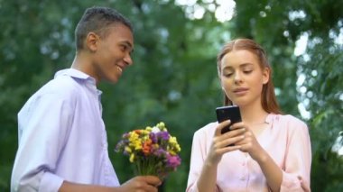 Kayıtsız genç kız erkek arkadaşı göz ardı çiçek sunan, sohbet akıllı telefon
