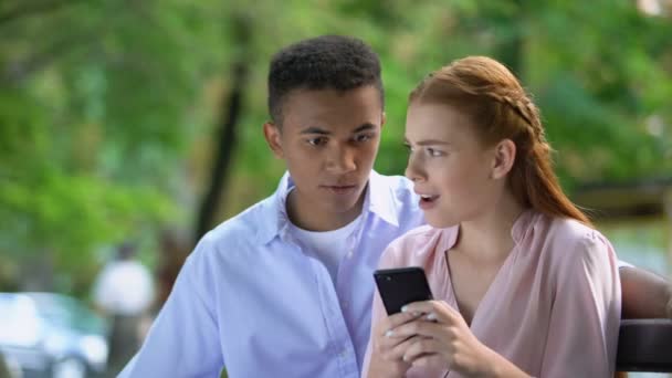 Chocado mestiço teen casal assistindo redes sociais fotos através de telefone — Vídeo de Stock