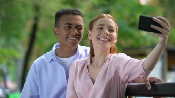 Sonriendo pareja adolescente divirtiéndose, haciendo fotos selfie en la cámara del teléfono inteligente — Vídeo de stock