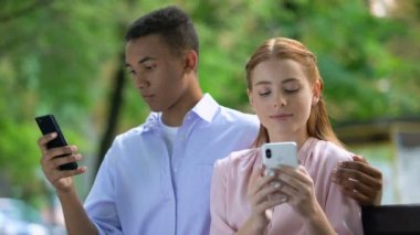 Parkta bankta oturan çok ırklı genç çift sarılma, sohbet akıllı telefon
