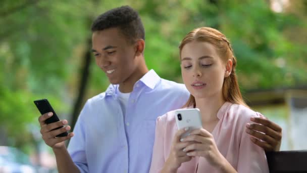 Beledigd meisje afkeer Afro-Amerikaanse vriendje chatten smartphone, jaloezie — Stockvideo