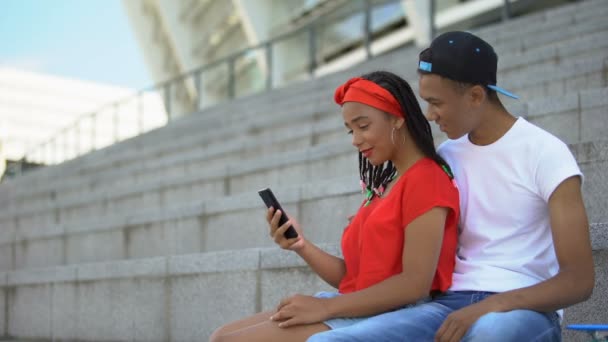 若いカップルは、ビデオを見て笑顔や携帯電話でソーシャルネットワーク上の投稿を読んで — ストック動画