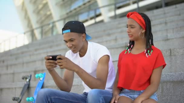 Захоплений гаджетом хлопець ігнорує свою дівчину, граючи в ігри на смартфоні — стокове відео