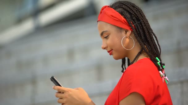 Stylish african american girl smiling into camera holding smartphone, leisure — Stock Video