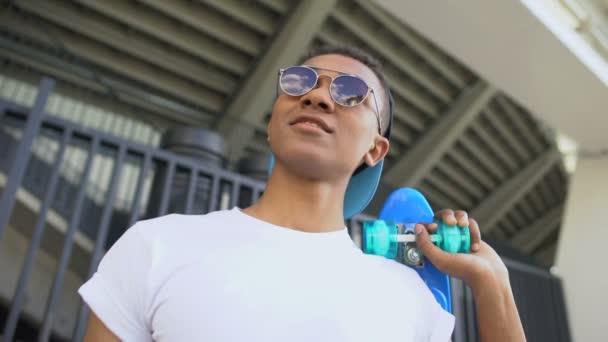 Mixed-Race Hooligan mit Sonnenbrille und Skateboard zum Abhängen bereit, Jugend — Stockvideo