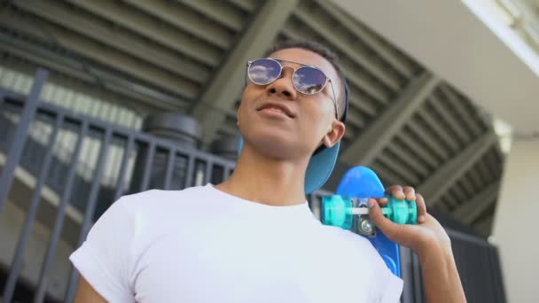 Mixed-race hooligan in sunglasses with skateboard ready for hanging-out, youth — Stock Video