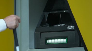 Baston ve görme bozukluğu olan yaşlı bir adam ATM 'ye kredi kartı sokmaya çalışıyor.