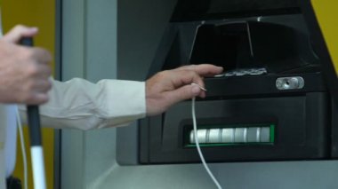Para çekmek ve bankacılık için kulaklıkları ATM 'ye bağlamaya çalışan kör kıdemli adam.