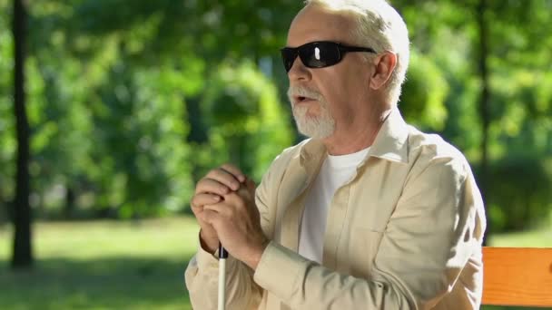 Triste vieil homme avec canne et lunettes sombres pensant sur banc, manque de soutien de l'État — Video