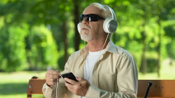 Сліпа людина намагається підключити кабель навушників до смартфона для прослуховування музики — стокове відео