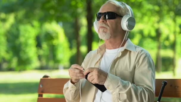 Зрелый человек с проблемами со зрением, подключение наушников и передача голосовой команды, приложение — стоковое видео