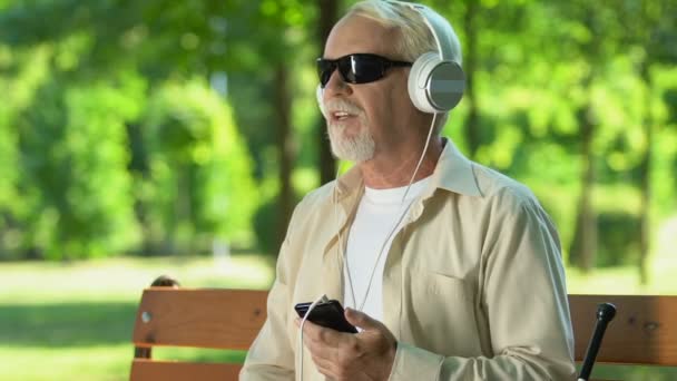 Старший чоловік з вадами зору насолоджується, слухає музику в навушниках — стокове відео