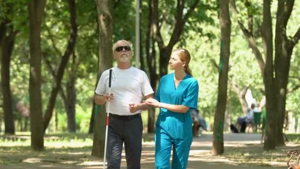 Enfermeira andando com o velho cego ao longo do parque de hospício, cuidados com a propriedade e apoio — Vídeo de Stock