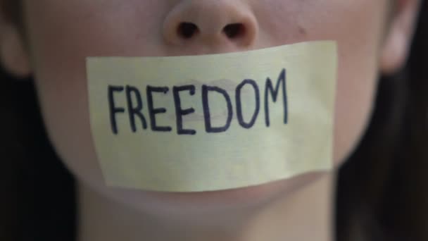 Freedom written on tape, woman removing mouth sticker, rights oppression, block — Wideo stockowe