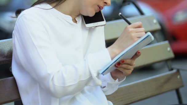 Businesswoman making notes talking phone sitting city bench, busy work lifestyle — ストック動画