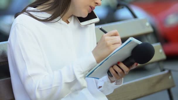 Young female journalist writing notebook talking on phone holding microphone — 비디오
